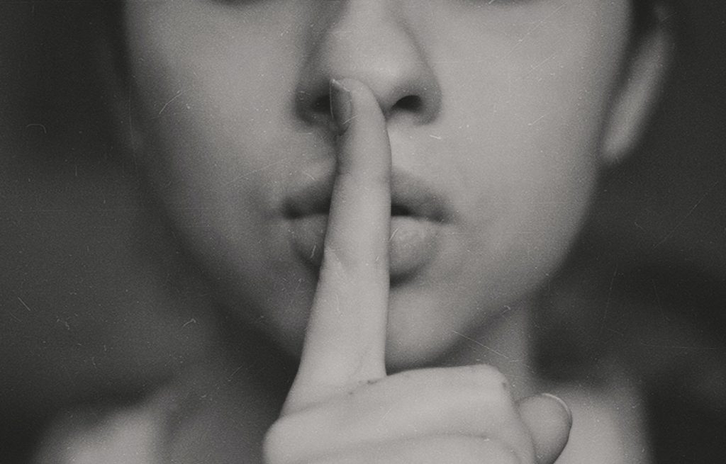 Woman covers her mouth with her finger, illustrating that good leadership involves being quiet and knowing when to delegate.
