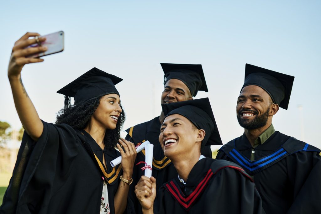 A group of college graduates take a selfie, illustrating the decision in IT hiring to look for a college graduate as a software developer.